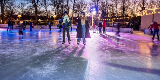 Flera personer åker skridskor på Stora isbanan i Folkets Park, med färgglada ljus i bakgrunden.