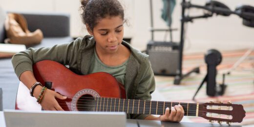 Ung tjej som spelar gitarr med instruktioner från en dator.