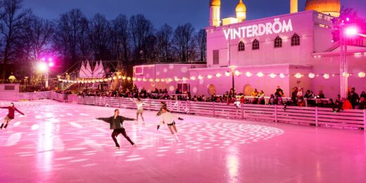 Ett antal personer åker skridskor på Stora isbanan i Folkets Park. I bakgrunden syns ett rosa ljus som lyser upp isen.