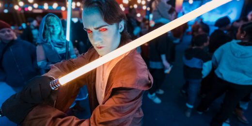 En person som cosplayar som en Star Wars-karaktär och håller upp en ljussabel mot kameran.